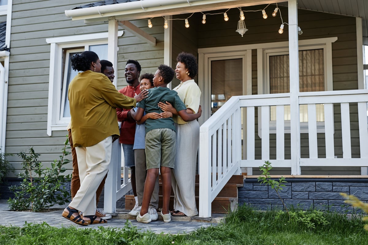 Happy Black family embracing on the porch of their new house — representing the dignity and stability Faith Anchored Housing provides